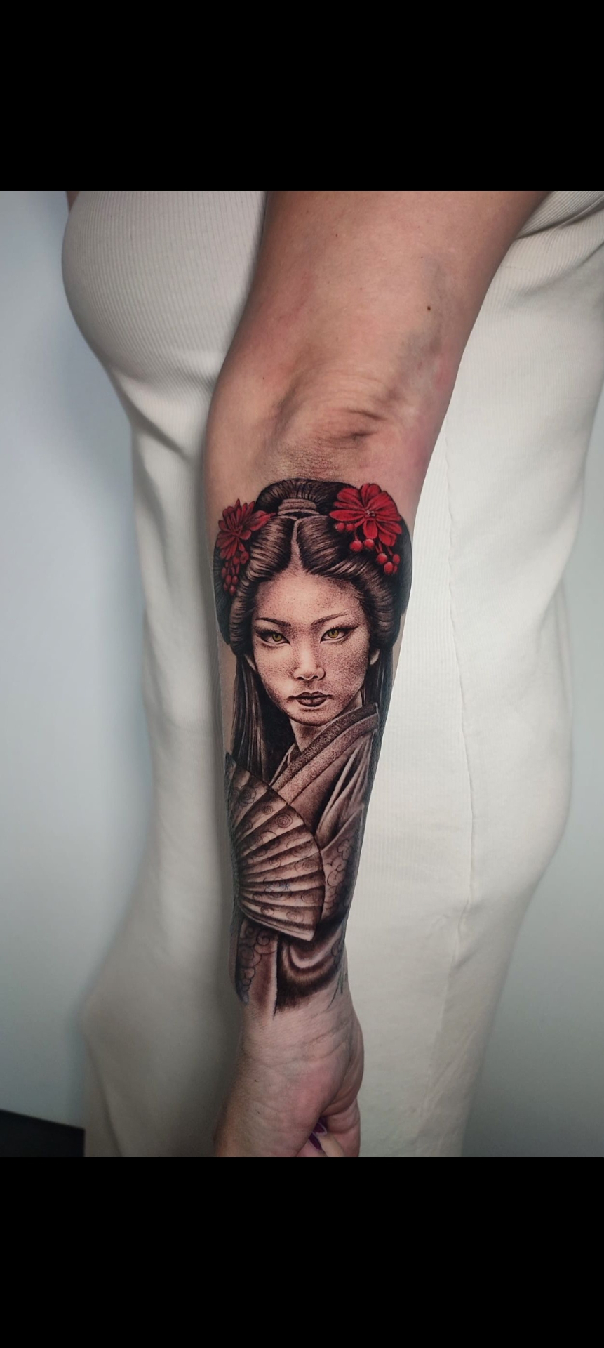 Tatuaje realista de geisha japonesa con flores rojas en el antebrazo — estilo realismo en Madrid centro · As de Picas Madrid